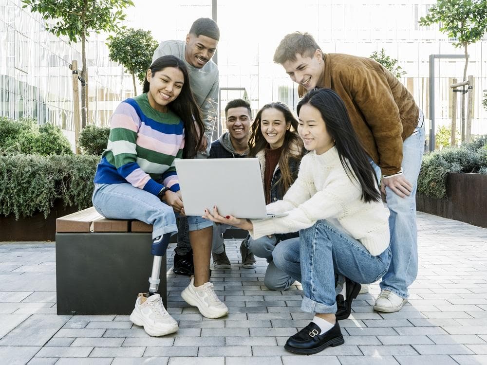 Group of smiling students looking at a laptop