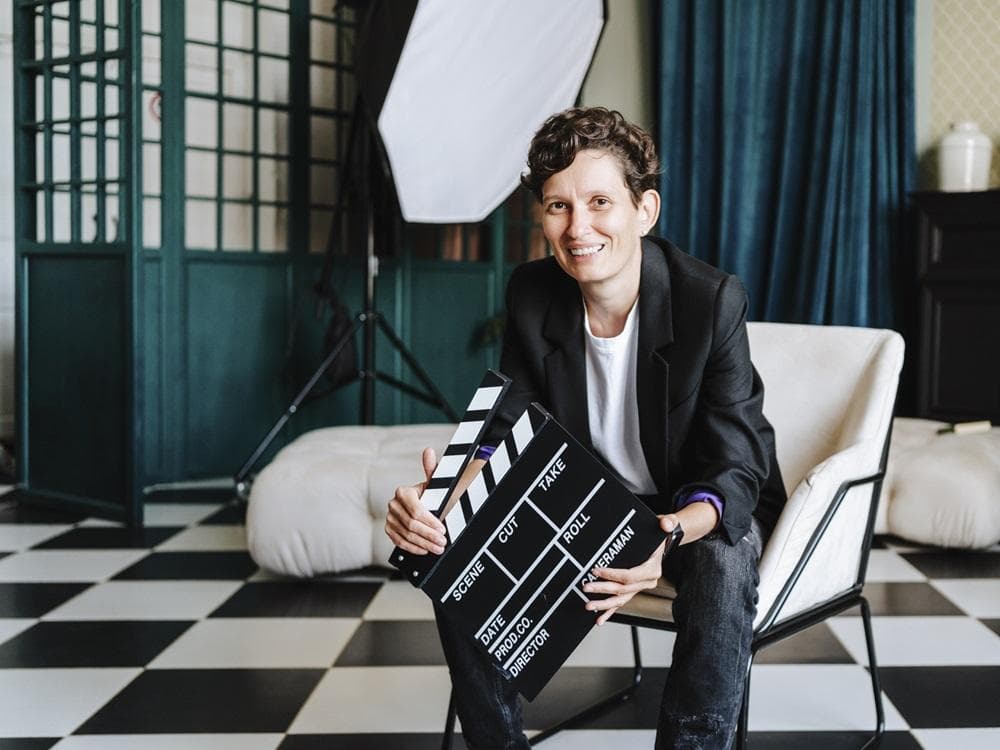 Smiling director sitting on chair holding clapboard on film set