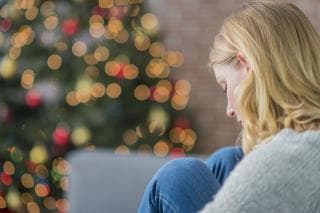 A woman sits alone near a Christmas tree