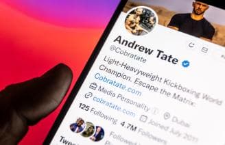 man holding mobile phone looking at Andrew Tate's twitter profile