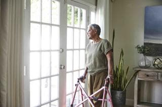 Older woman using a walker, looking out of a window