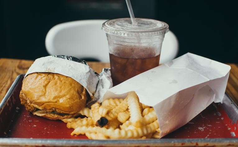 Fast food, including a burger and fries, on a tray in a restaurant.