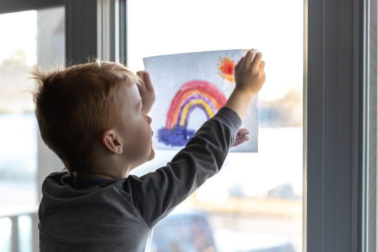 A boy sticks a poster of a rainbow to a window