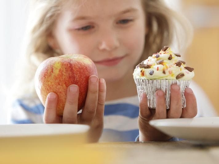 Girl choosing between an apple and a cake