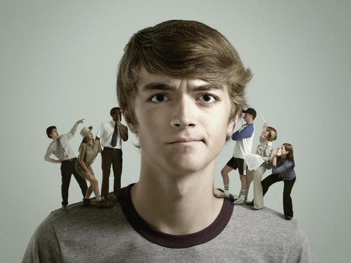 Young man with multiple people standing on each shoulder talking in his ears