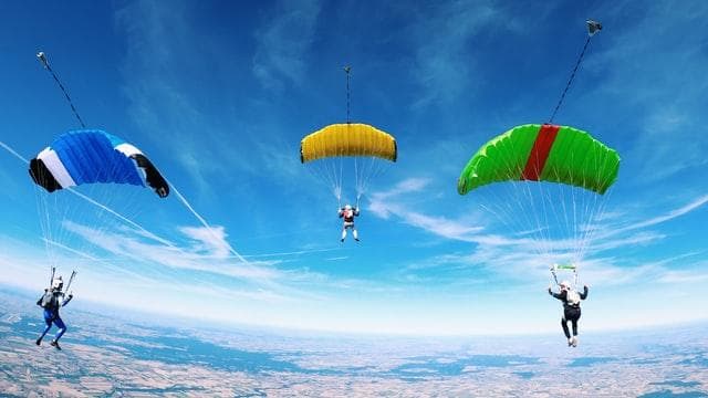 Three skydivers with parachutes in a blue sky