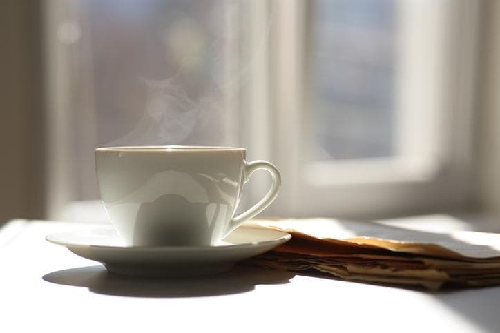 Coffee cup and newspaper on table in the sun