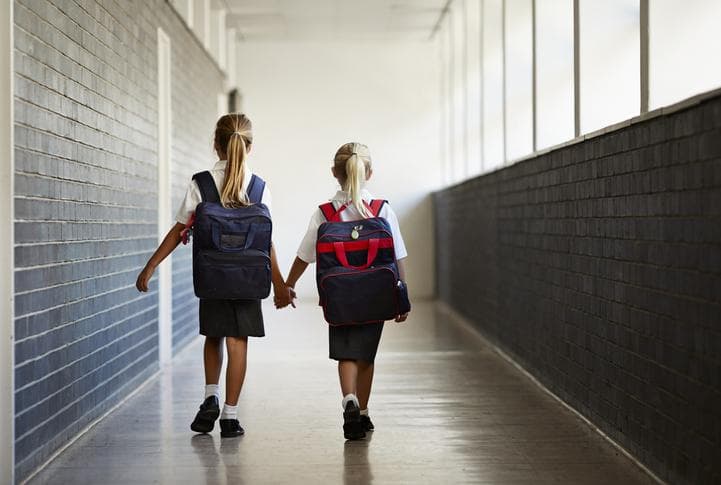 Two girls walking hand in hand down school corridor