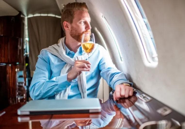 Wealthy man on an airplane drinking a glass of wine