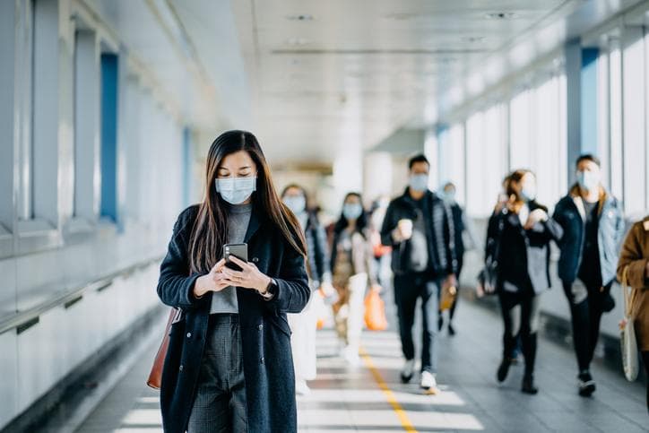 Woman wearing mask walking and looking at phone