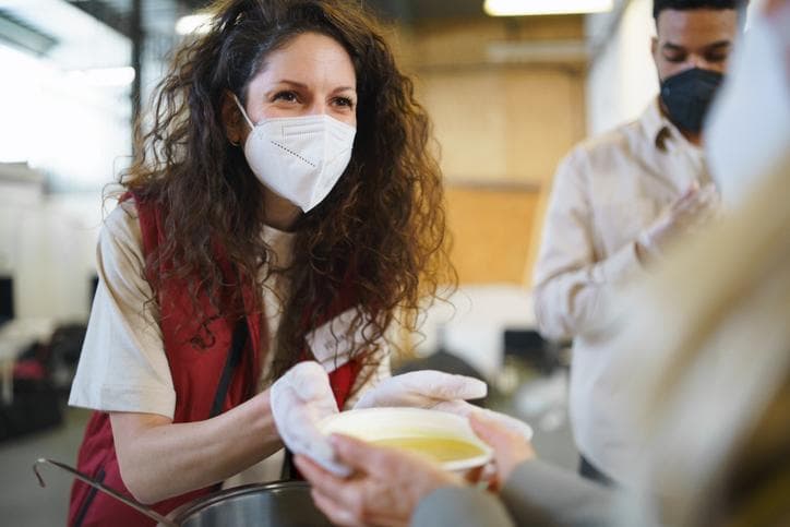 Woman with mask offering bowl of soup at community centre