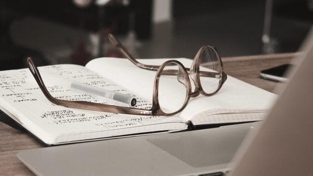 a pair of glasses on top of a notebook beside a laptop