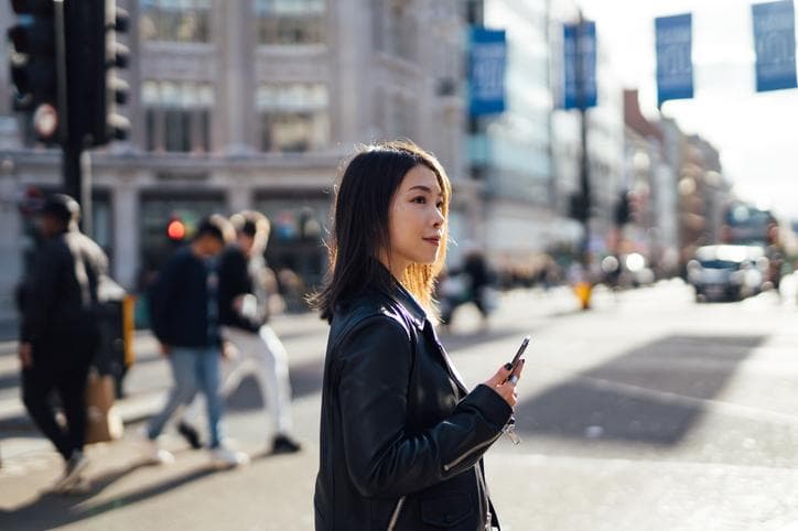 A woman holds her phone while in the street on a sunny day