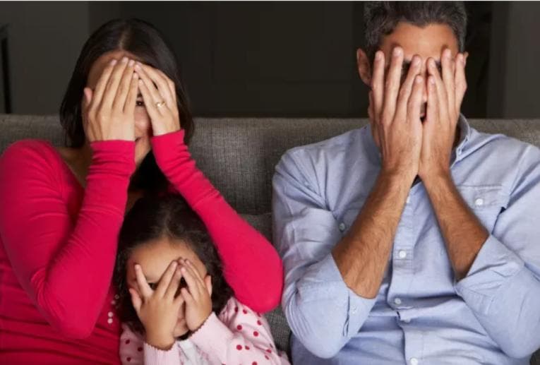 Parents and child watching a movie through their fingers