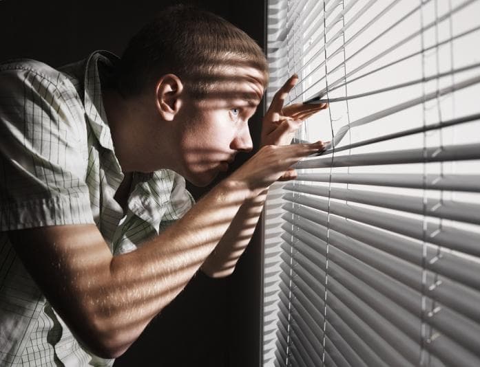 Suspicious man peering through blinds