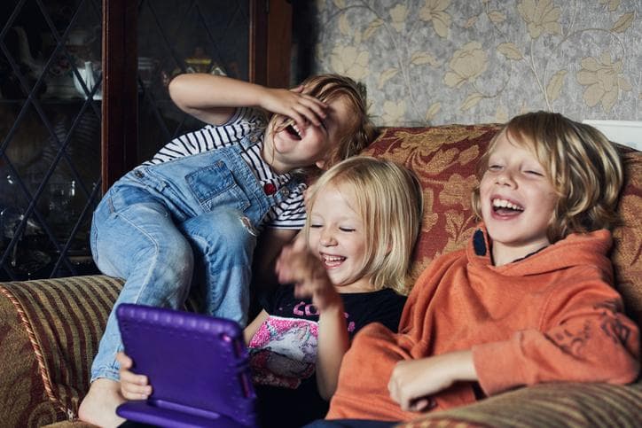 Three children sit together on a sofa and laugh