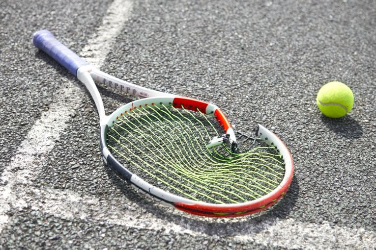 A broken tennis racket next to a ball