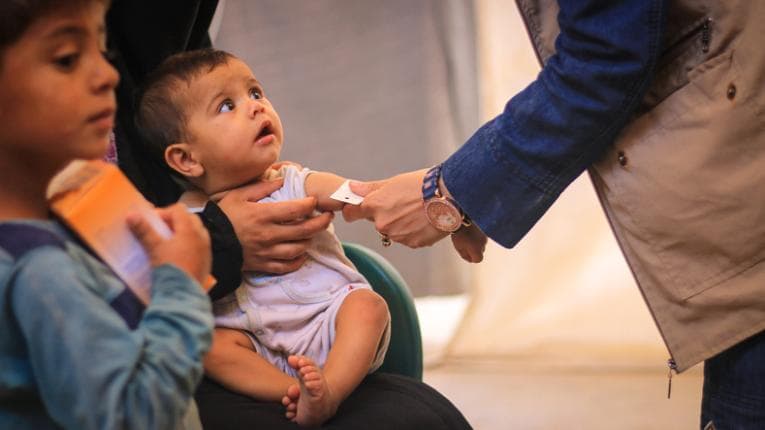 A baby is assessed by a worker helping refugees