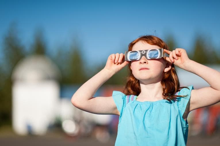 Girl watching solar eclipse through viewing glasses