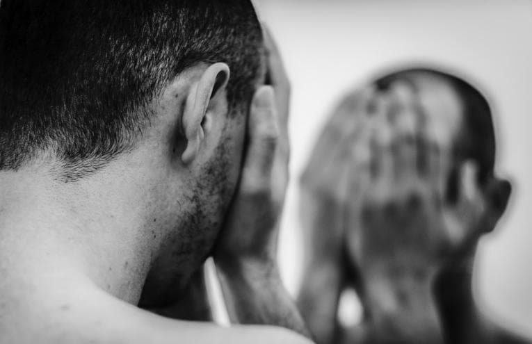 Man hiding his face while looking in mirror