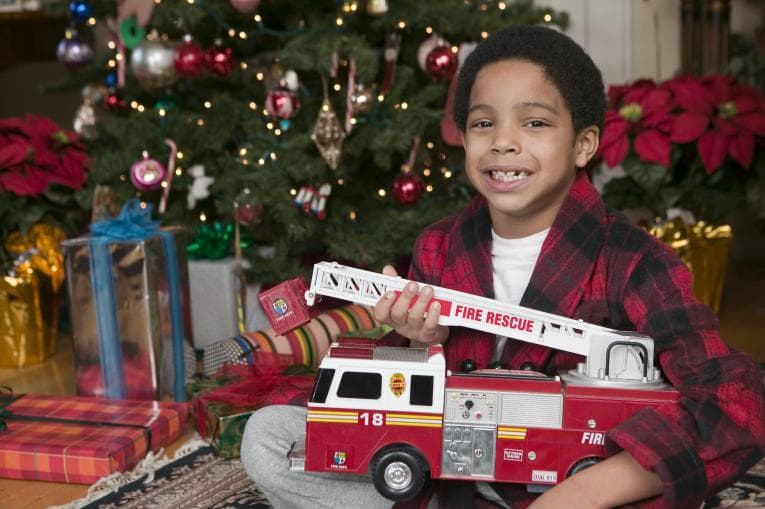 Smiling boy in front of Christmas tree holding toy fire engine