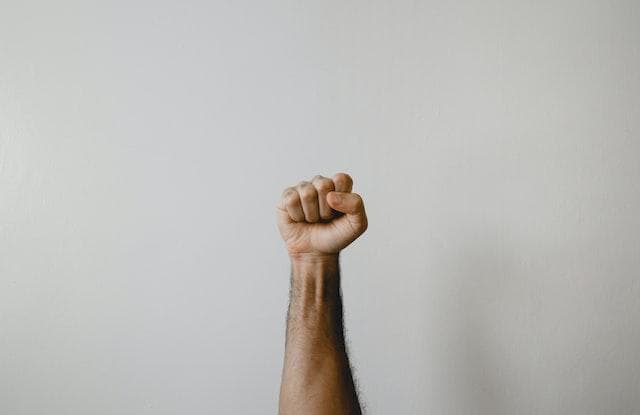 A man's arm and fist held in the air in front of a white background.