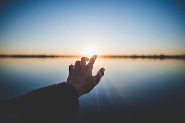 Hand reaching towards sunrise