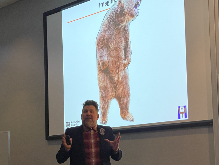 Mark Wetherell presenting with image of bear behind him 