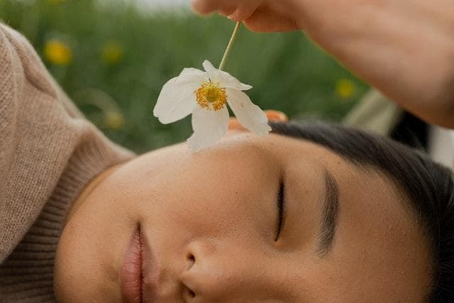 Woman lying on side with eyes closed being tickled on face with a flower