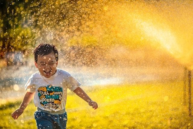 Young boy running through sprinkler laughing