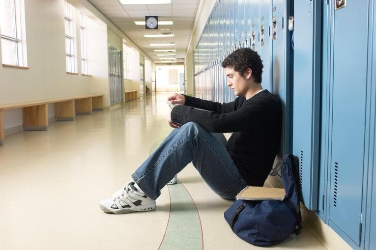 Boy sitting against lockers in school hallway