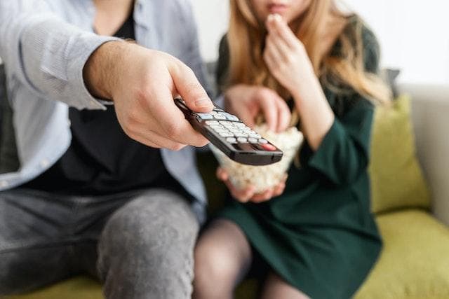 Couple eating popcorn and pointing remote at TV