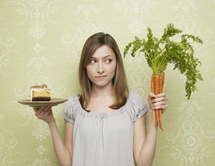 Person holding a plate of cake in one hand and carrots in the other