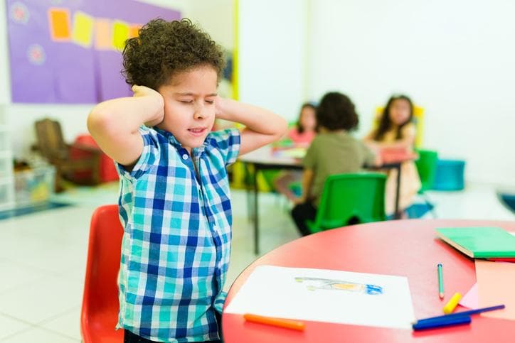 Child in classroom covering ears