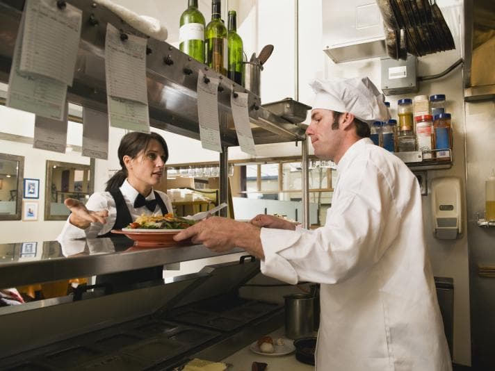 Waitress taking dish from chef