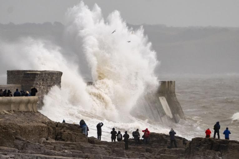 Huge waves crashing over pier as people watch