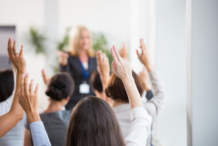 Audience with raised hands facing speaker in office environment